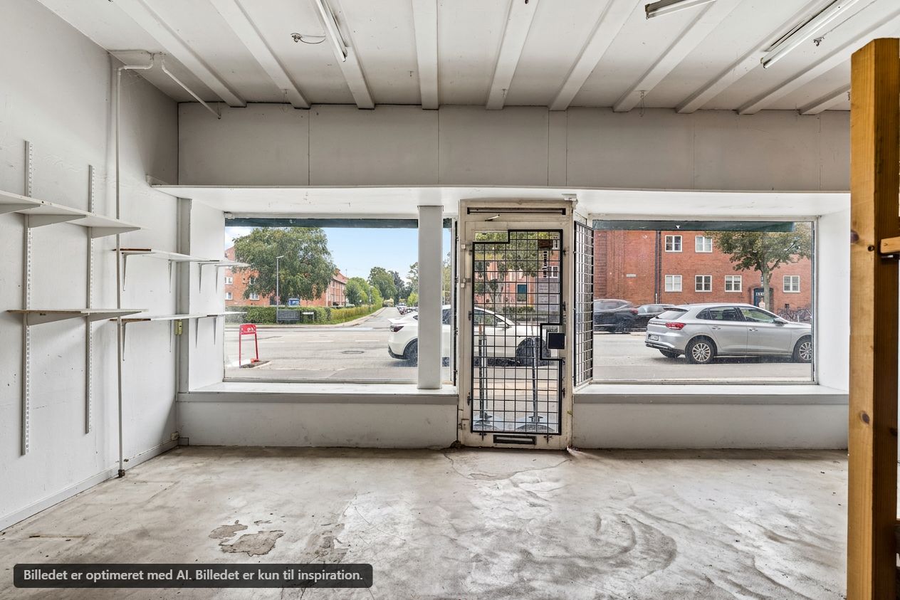 Et tomt butikslokale med store vinduer og indgangsdør i st. th på Frederikssundsvej. Bygningen er uden inventar og har hvide vægge med indbygget hyldesystem.
