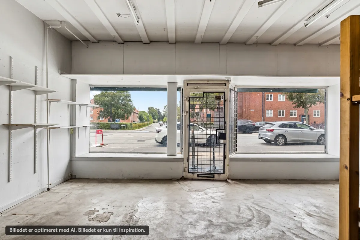 Et tomt butikslokale med store vinduer og indgangsdør i st. th på Frederikssundsvej. Bygningen er uden inventar og har hvide vægge med indbygget hyldesystem.