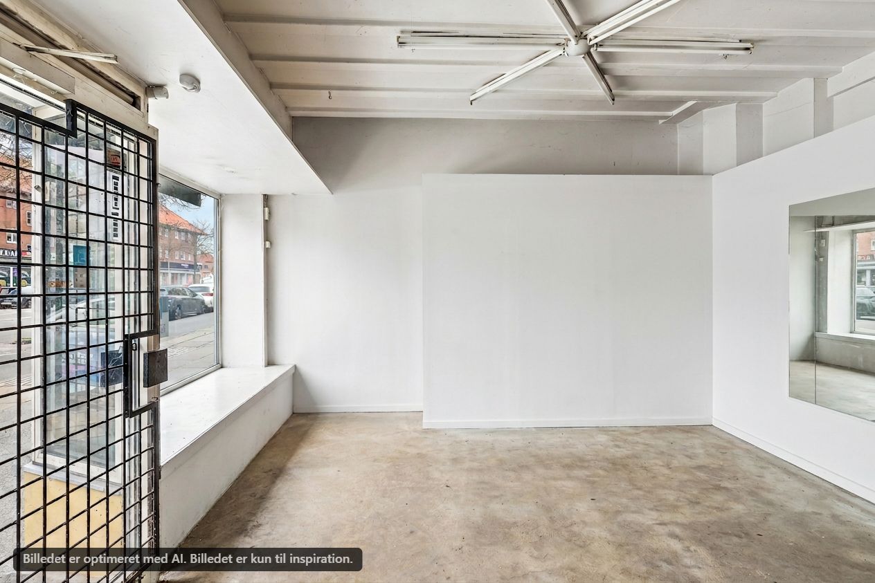 Erhvervsandel til salg i Brønshøj med en stor butiksfront og indvendig vinduesvisning. Store hvide vægge og en kontordel med glasvægge. Lejligheden er nyrenoveret med moderne indretning og er ideel til mindre virksomheder