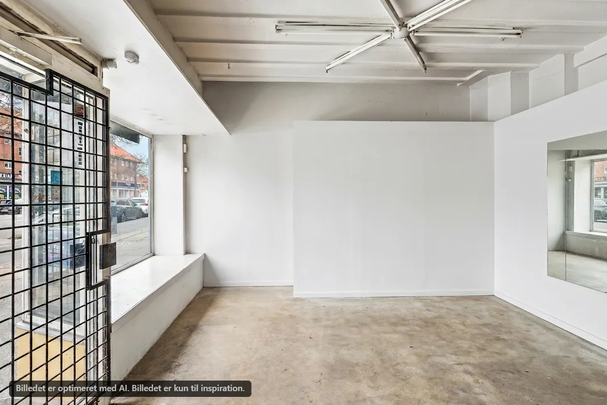 Erhvervsandel til salg i Brønshøj med en stor butiksfront og indvendig vinduesvisning. Store hvide vægge og en kontordel med glasvægge. Lejligheden er nyrenoveret med moderne indretning og er ideel til mindre virksomheder