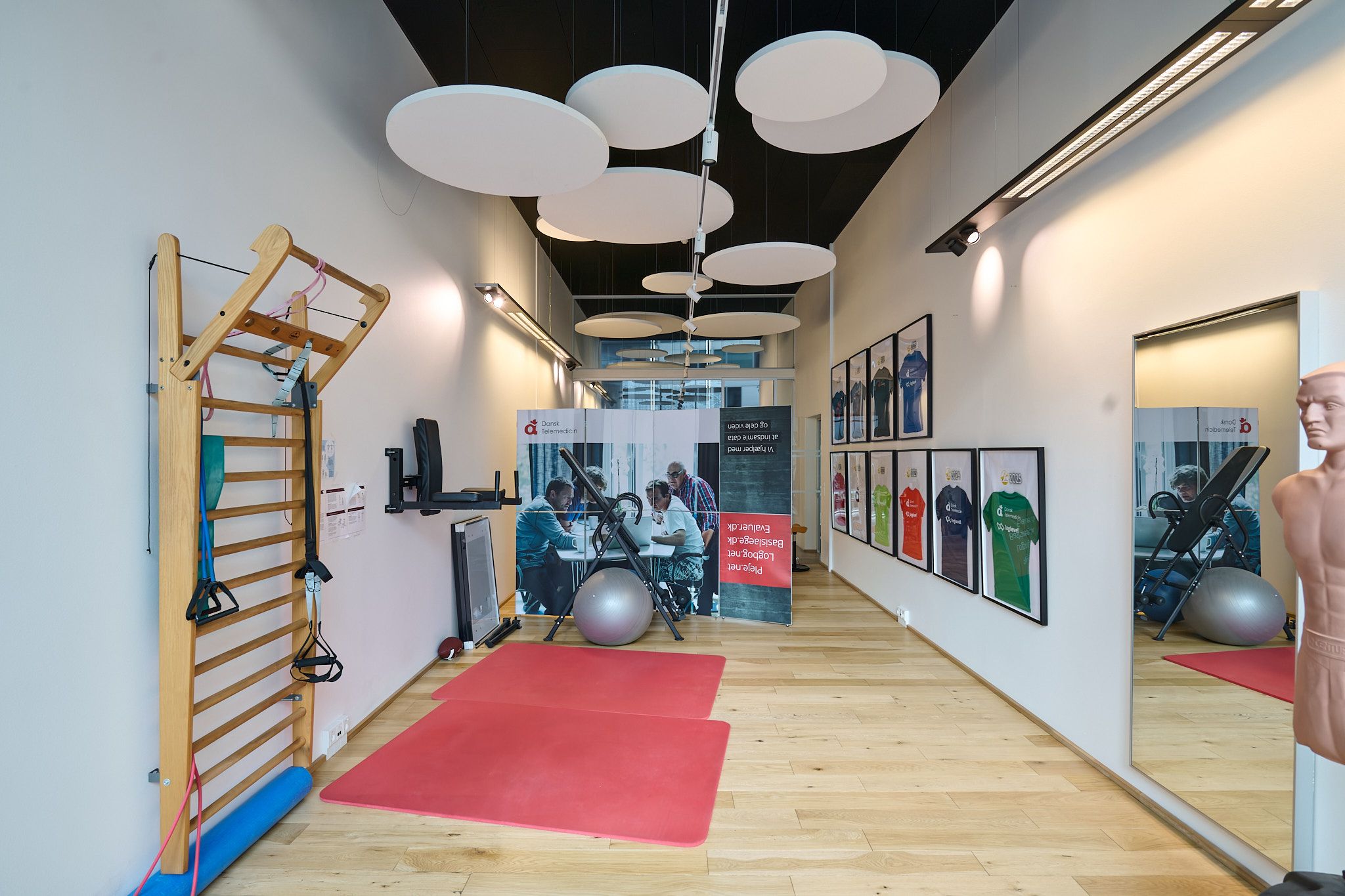 En moderne og veludstyret fitness- og yogastue med trægulve, røde yogamåtter, træpullupstang, baller og spejl.