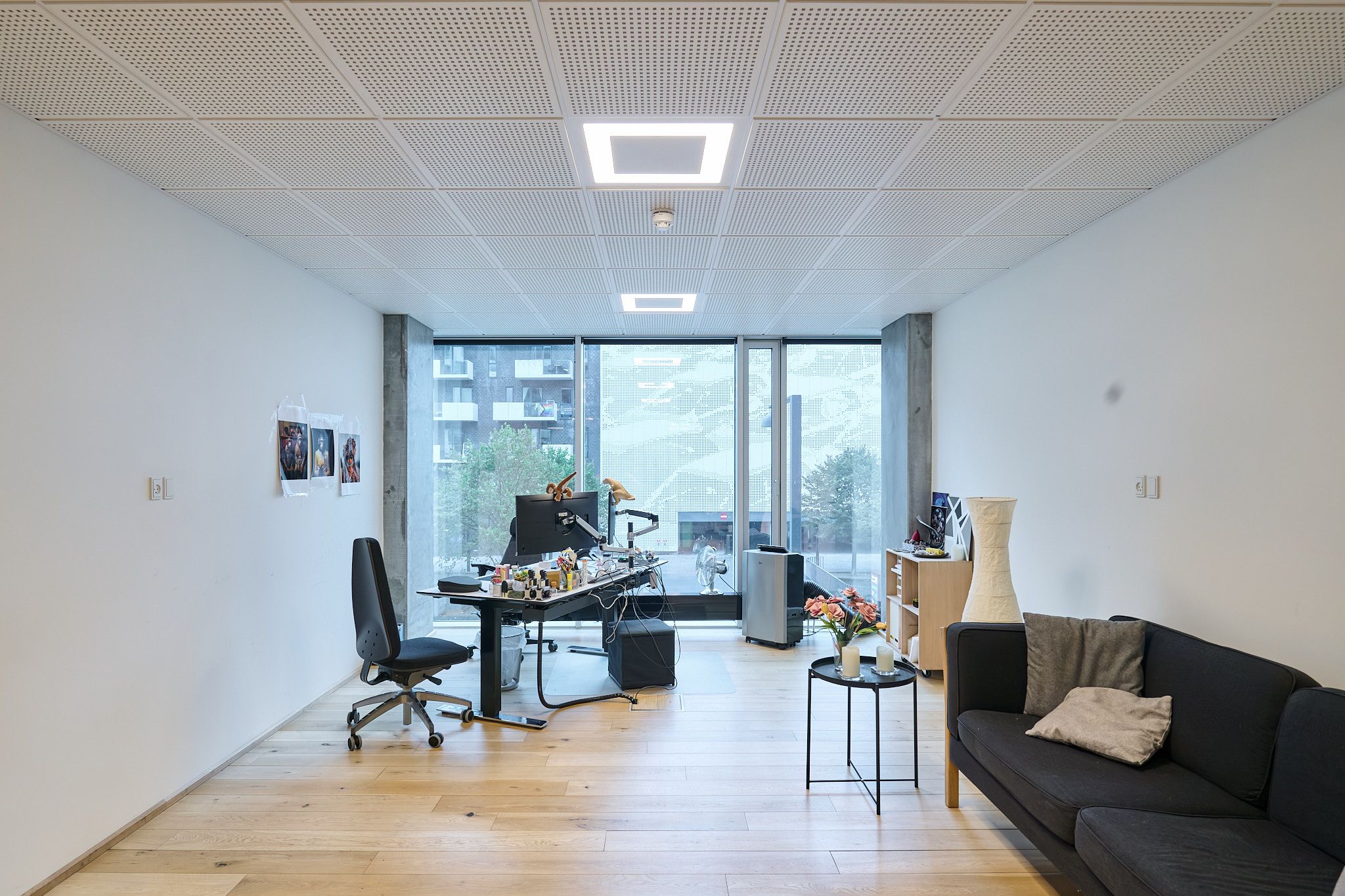 Kontor med masser af lys, højloft, moderne skrivebord, stol, sofa og blomster på sidebordet
