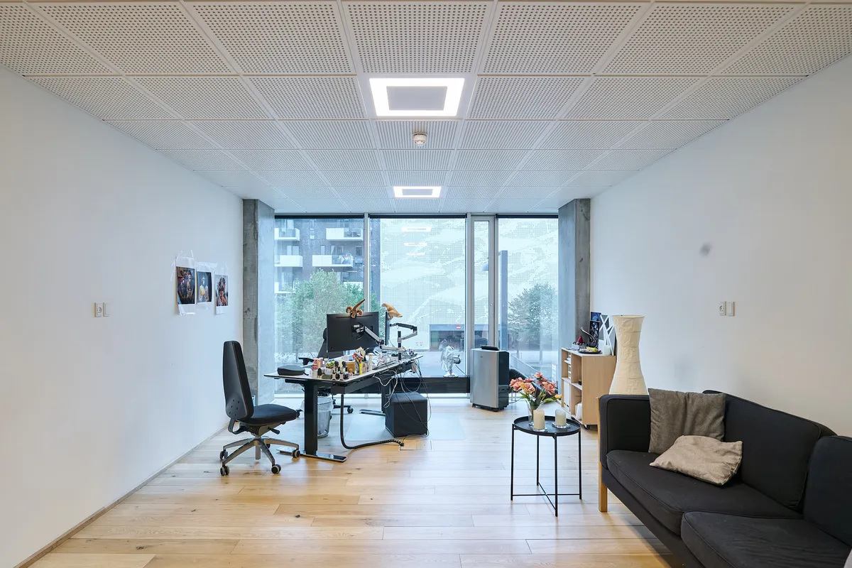 Kontor med masser af lys, højloft, moderne skrivebord, stol, sofa og blomster på sidebordet