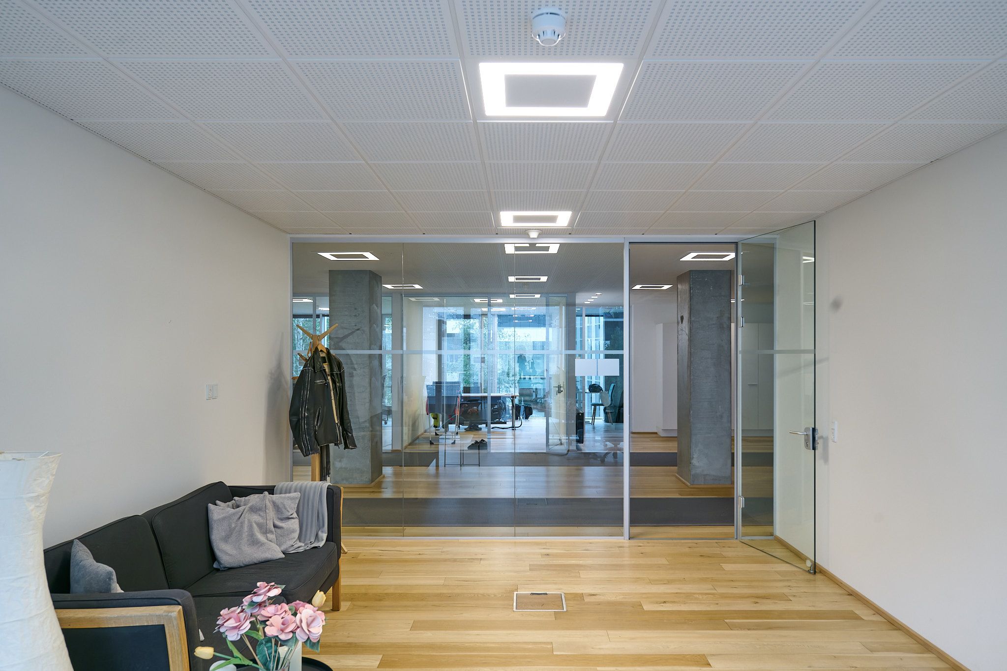Kontorlokaler med moderne interiør, glasvinduer og højloft, hvidt loftsdesign, hårdt trægulv, møbler og dekorationer, ligesom en sofa med tæpper og en lysekron