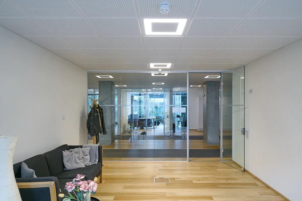 Kontorlokaler med moderne interiør, glasvinduer og højloft, hvidt loftsdesign, hårdt trægulv, møbler og dekorationer, ligesom en sofa med tæpper og en lysekron