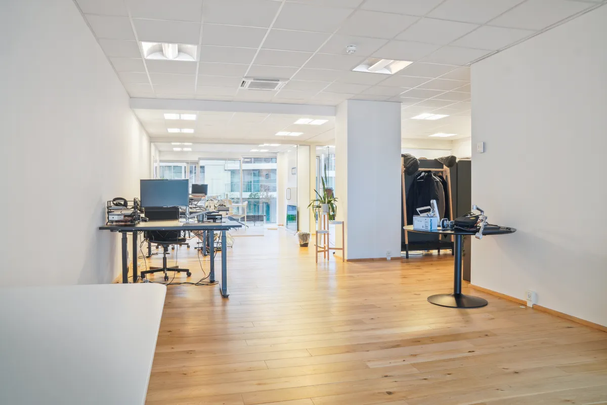 Moderne kontor med højloft, smukke trægulve og funktionelle skriveborde. Styrende belysning og minimalistisk indretning med grønne planter.