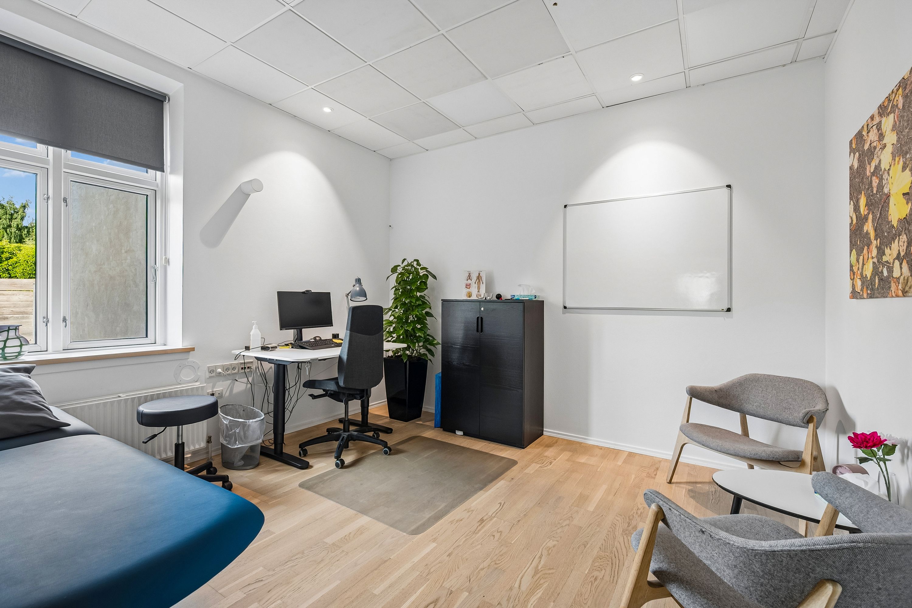 Kontor med højt loft og hvide vægge med en hvid tavle og et skrivebord med computer, plante og stol samt møbler og tavle med en røg blomst