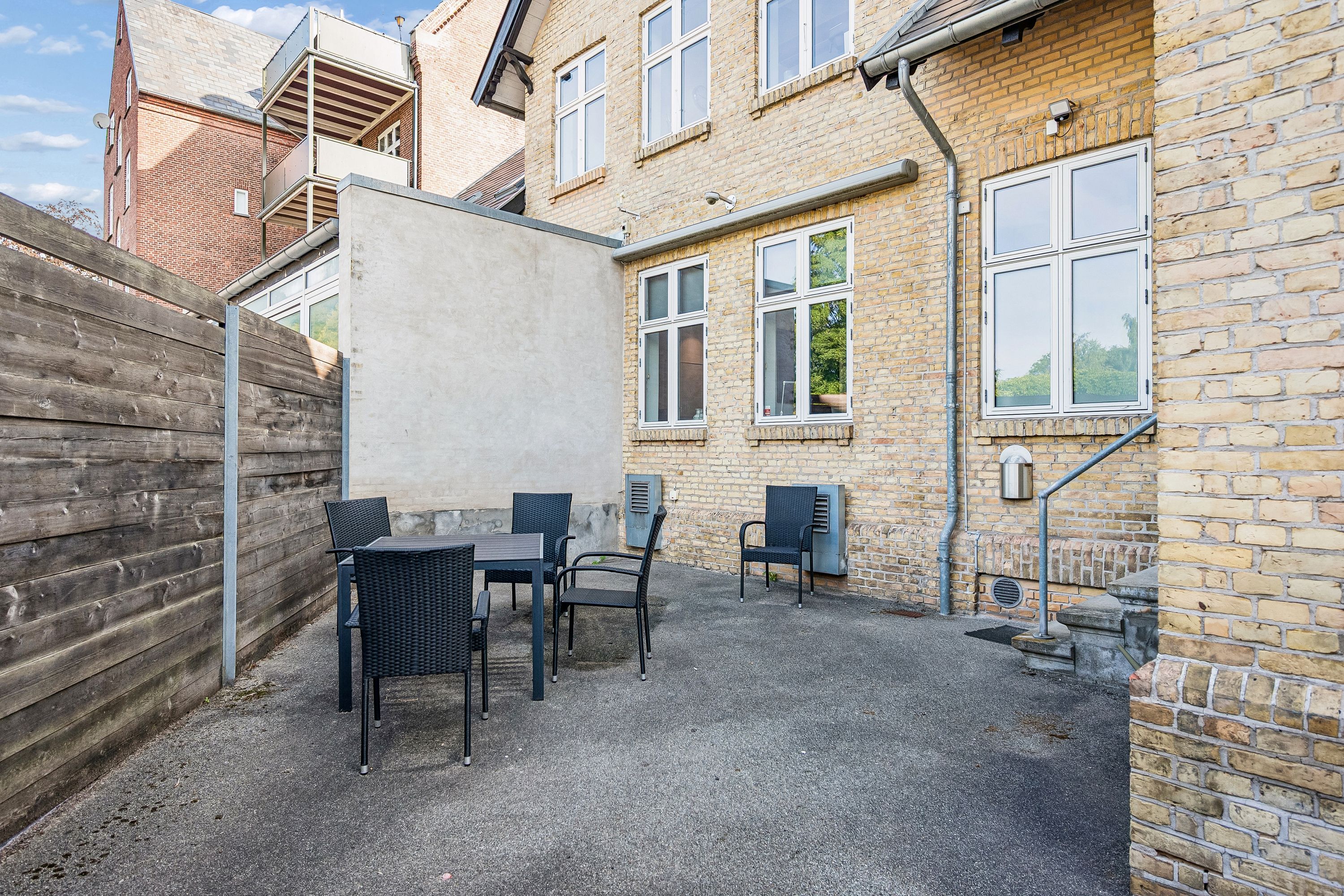 Kontor i Lyngby med en lille terrasse, hvor der er stillet en rundt bord og fire møbler. Murene er lavet af røde mursten og der er en høj stående kasse til rør.