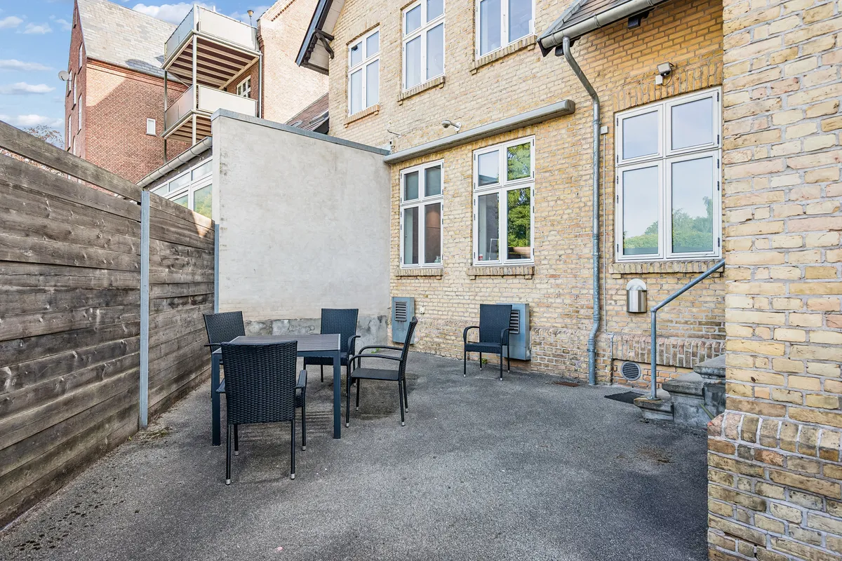 Kontor i Lyngby med en lille terrasse, hvor der er stillet en rundt bord og fire møbler. Murene er lavet af røde mursten og der er en høj stående kasse til rør.