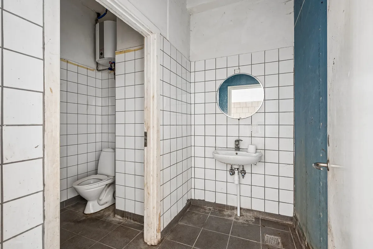 Moderne toiletrum med gult og hvidt flisebelagt væg og gulv samt hvidt toilet og sæbeholder over vasken.