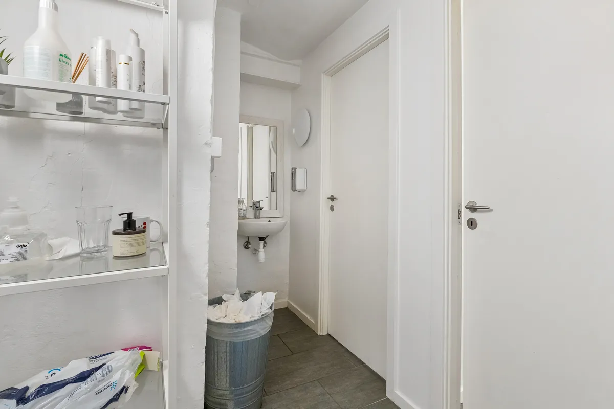 Rent, rent toilet med håndvask og spejl, opbevaringsskabe med kosmetik og toiletartikler samt papposer og skraldespand i gulvet