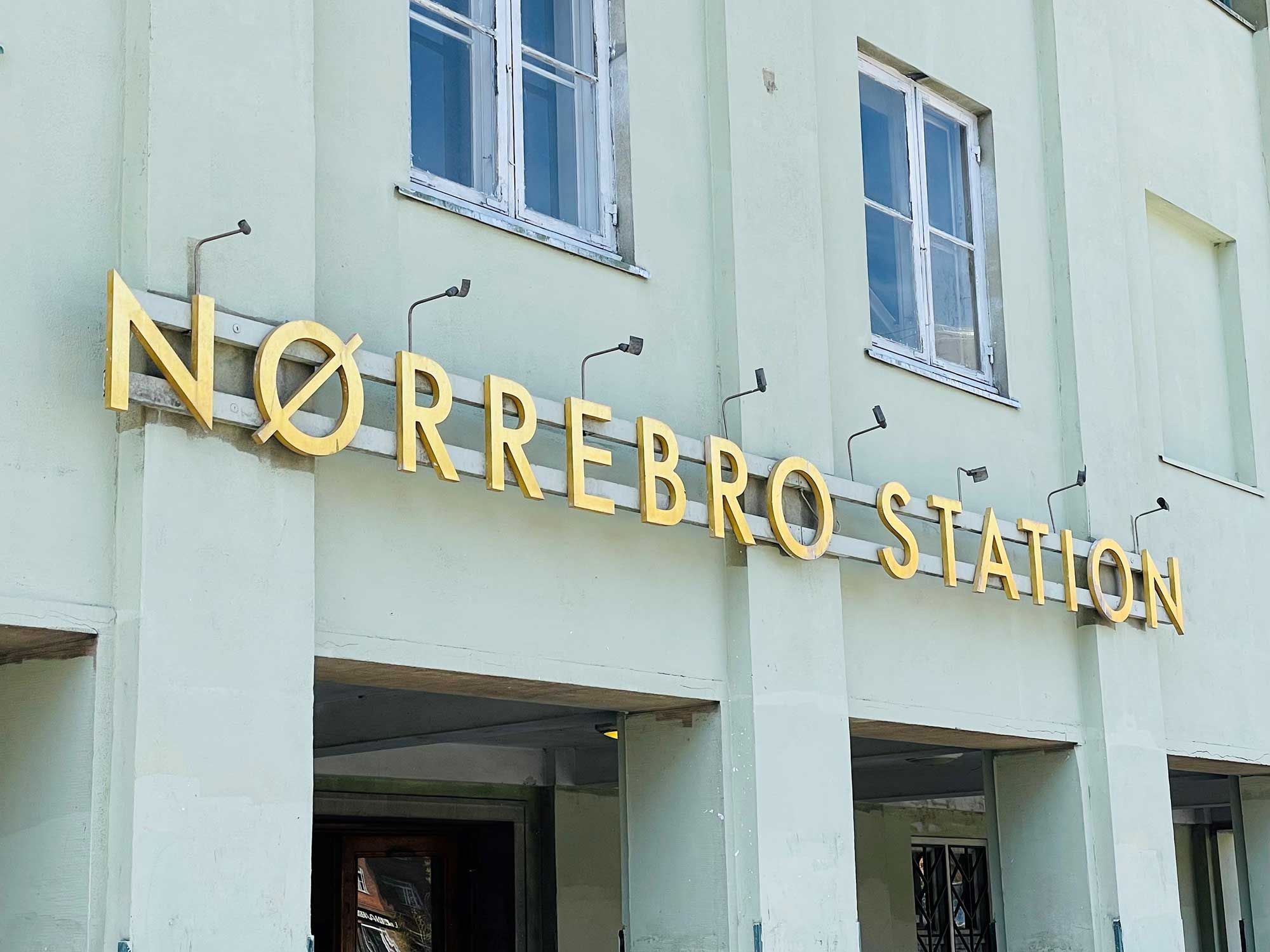 Foto af Nørrebro station med indgang, gule bogstaver og tre vinduer med hvide ruder