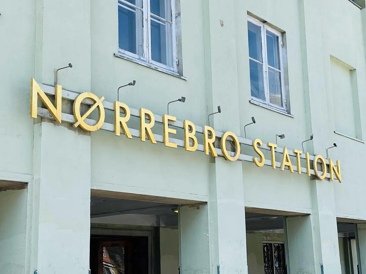 Foto af Nørrebro station med indgang, gule bogstaver og tre vinduer med hvide ruder