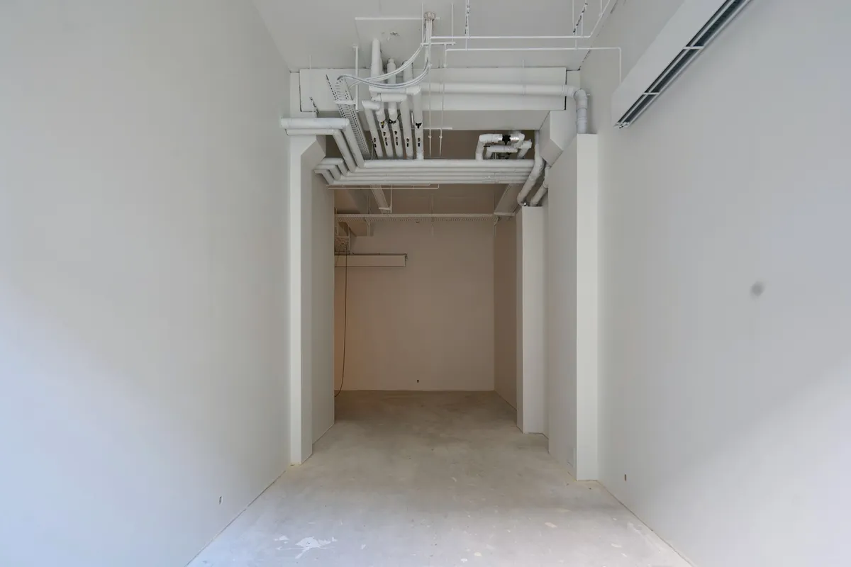Kort og klar lejetjeneste til detailhandel med store, hvide vægge og gulv samt hængende, hvide rørstel. Det er en lukket gang, hvor der er udstillingsmuligheder.