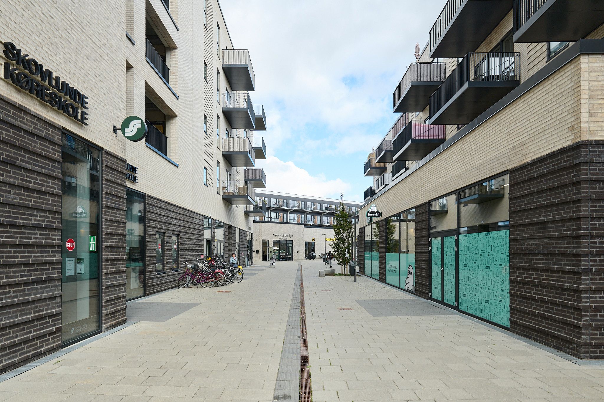 Skovlunde skole og lejemål på Torvestrædet. Strædet er tomt for folk, og der er parkerede cykler ved siden af butikkerne.