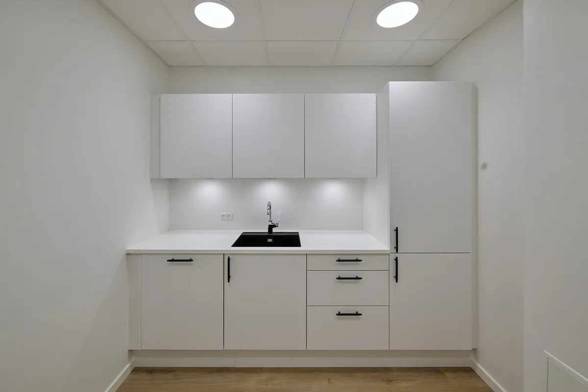 En minimalistisk køkken med hvide vægge, hvide skabe og et sort tællebord med en vandhane i sølv