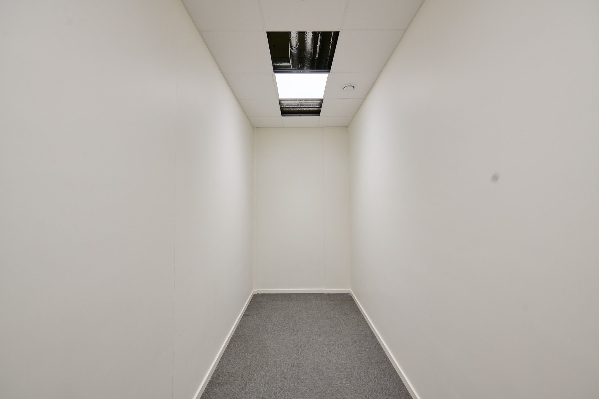 Et funktionelt erhvervslejemål med hvidmalede vægge og gulvbelægning. Lejligheden er ubeboet og har lyse lofter med et slankt vinduesfelt.