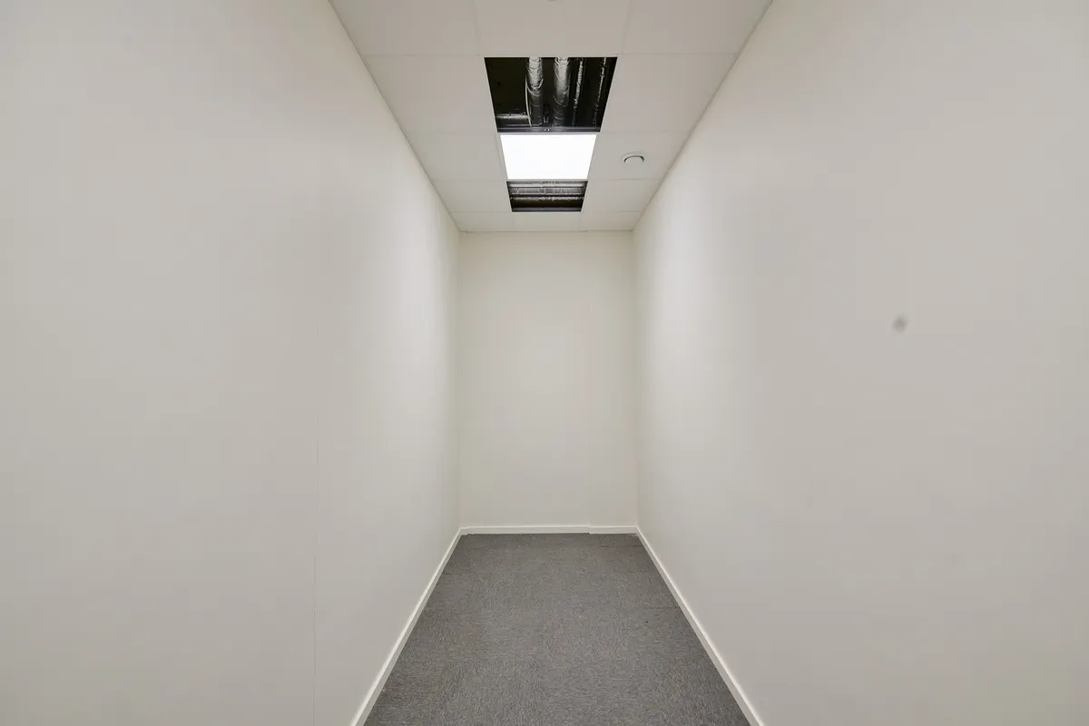 Et funktionelt erhvervslejemål med hvidmalede vægge og gulvbelægning. Lejligheden er ubeboet og har lyse lofter med et slankt vinduesfelt.