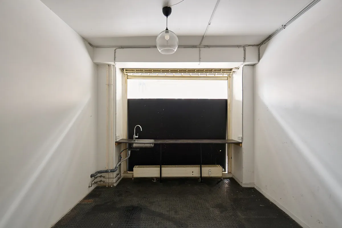 En tom kontorrum med lyse hvide vægge, sort gulv og en lysegrå loft. En enkelt skålvask er fastgjort til væggen og en enkelt lampe hænger fra loftet