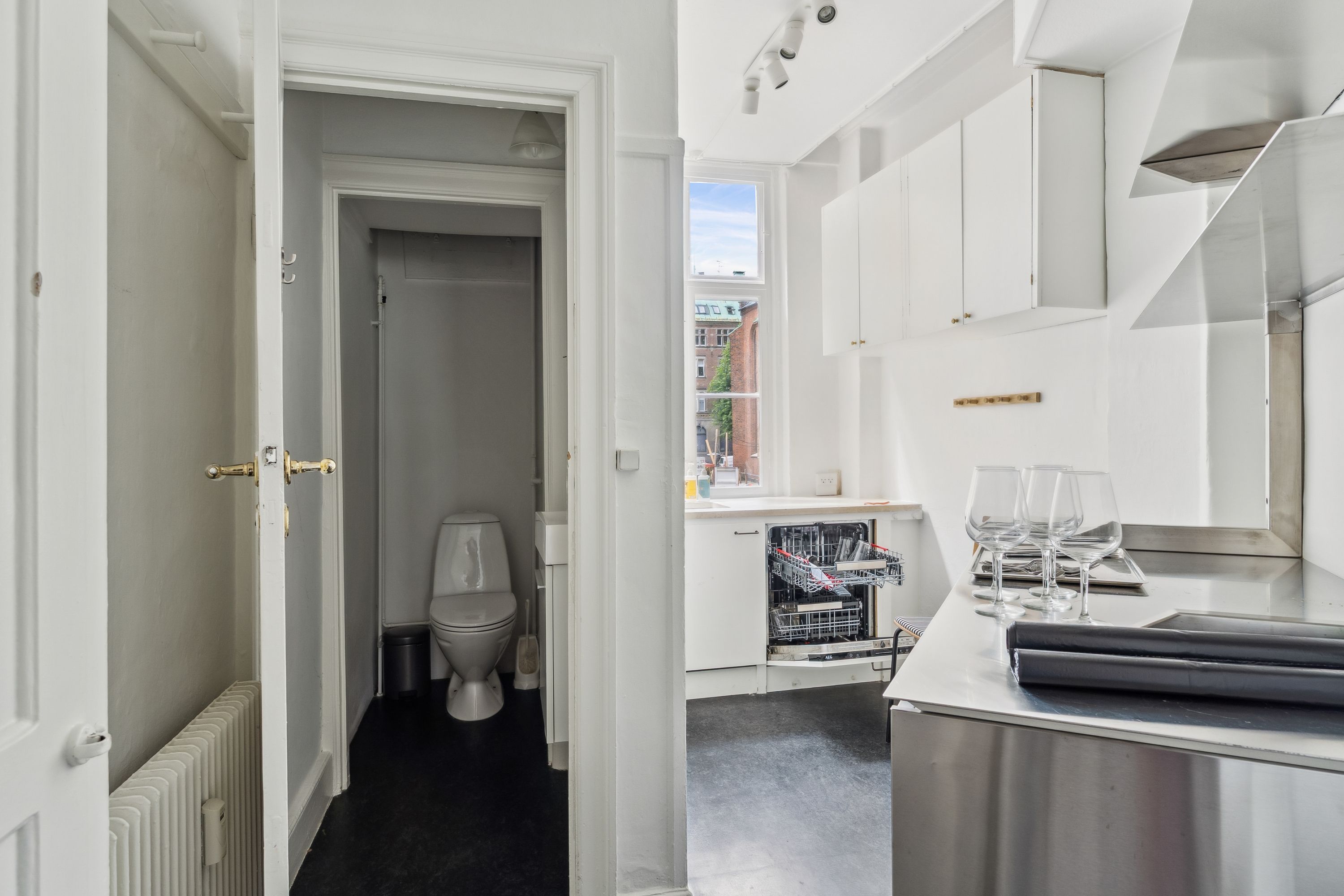 Moderne og pænt køkken med lyse farver og blanke overflader, vinglas og glasflader, lyskroner, toilet og radiator, samt opvaskemaskine og vinduesvisker