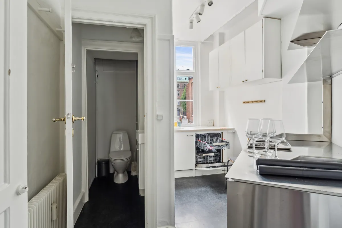Moderne og pænt køkken med lyse farver og blanke overflader, vinglas og glasflader, lyskroner, toilet og radiator, samt opvaskemaskine og vinduesvisker