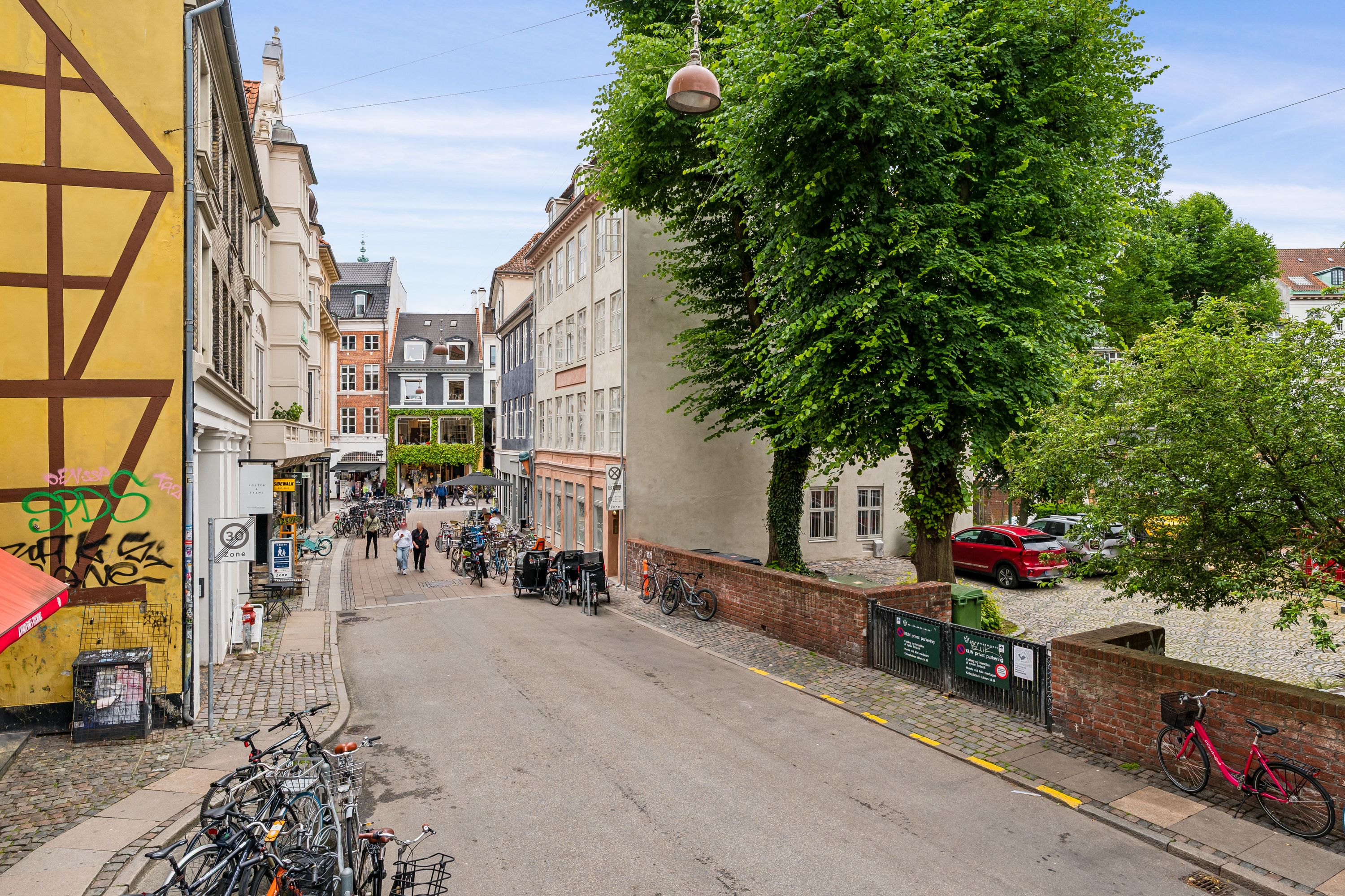 En trafikeret gade med cykler og biler i baggrunden, og en smal vej med en 30 km/t skilt