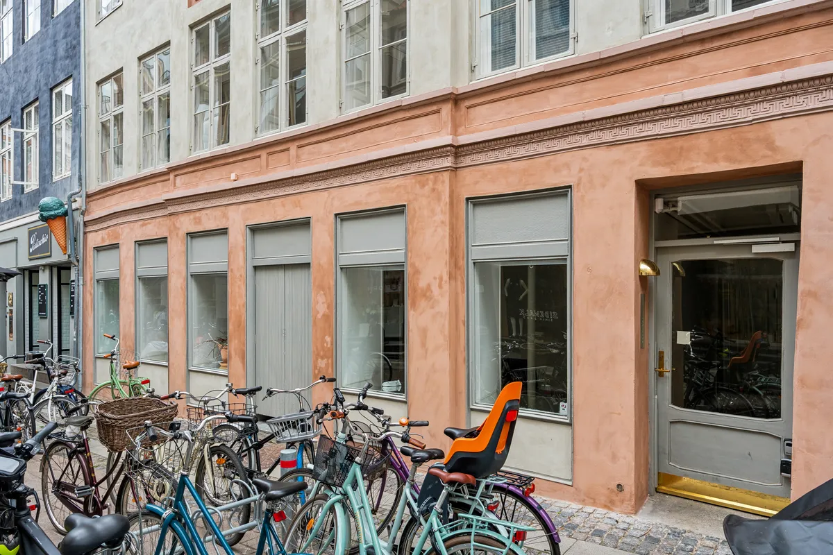 Butik i lysebrun bygning med møbelforretning, møbler og cykler parkeret udenfor og en isvogn i baggrunden