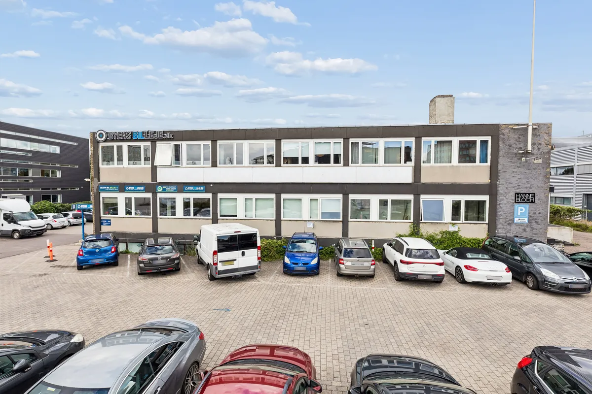 Kontorbyggeri med flere parkerede biler og et stort skriftstykke med teksten Hanne Bloch