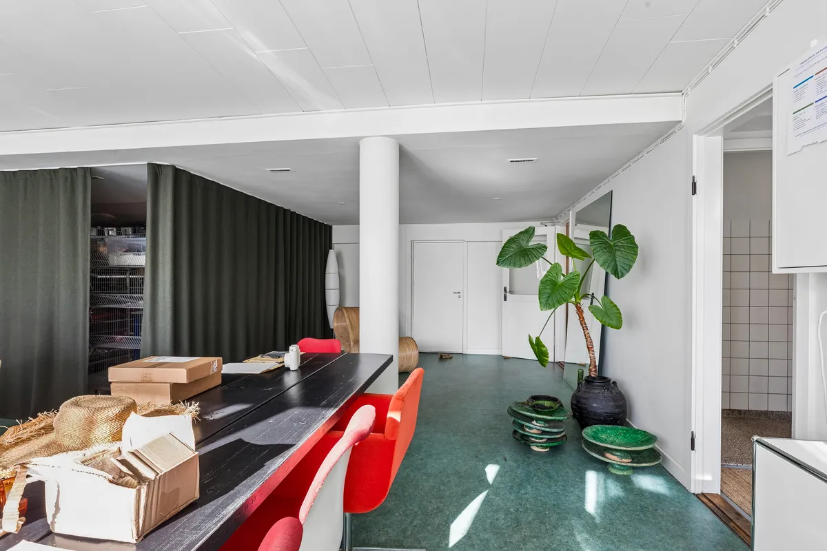Kontor med røde stole, møbler og grønne planter samt flere kasser og papkasser på et langt bord