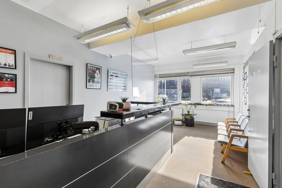 Kontor med moderne indretning, to skærme, plante og lyse lamper. To lysegrå stole og en åben dør.