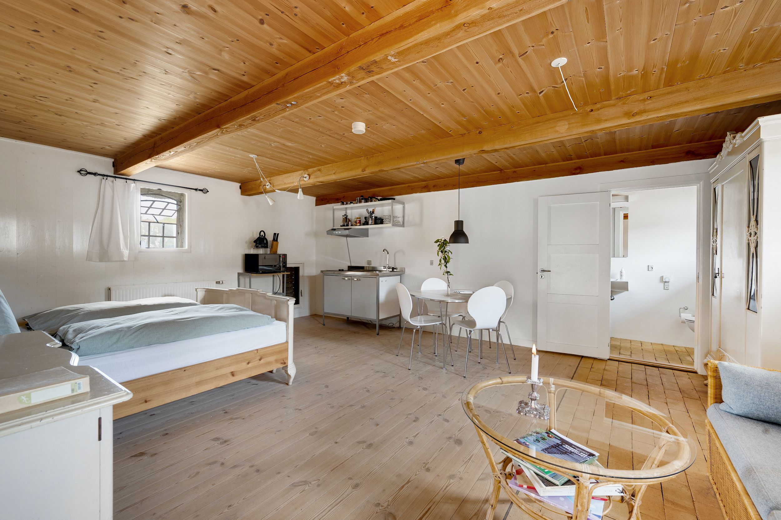 Elegant hyggeligt interiør med højt loft, åbent køkken med moderne faciliteter, hvidt bord med stole, trægulv og møbleret