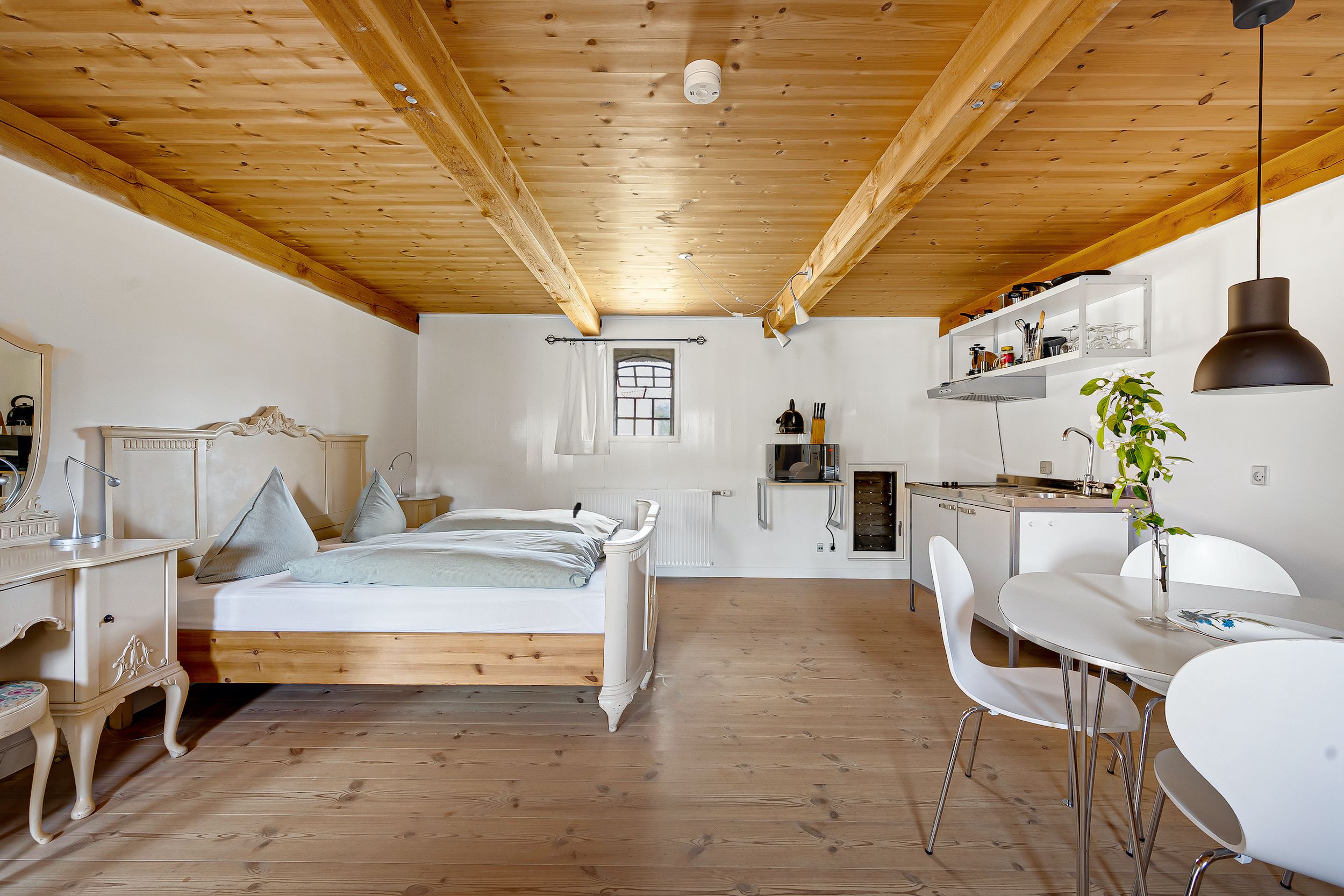 Hyggeligt soveværelse med dobbeltseng, lyse brædder på loftet og køkken med hvide vægge og lysegrå møbler