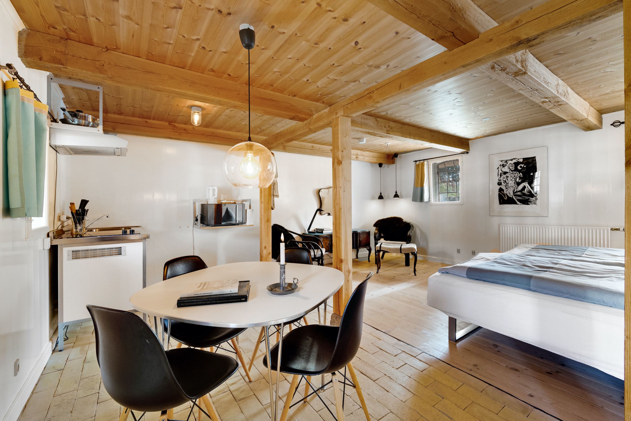 En hyggelig stue med en rund spisebord, fire stole, en senge, sofa, loftsbjælker, en lampe og en gulv i træ