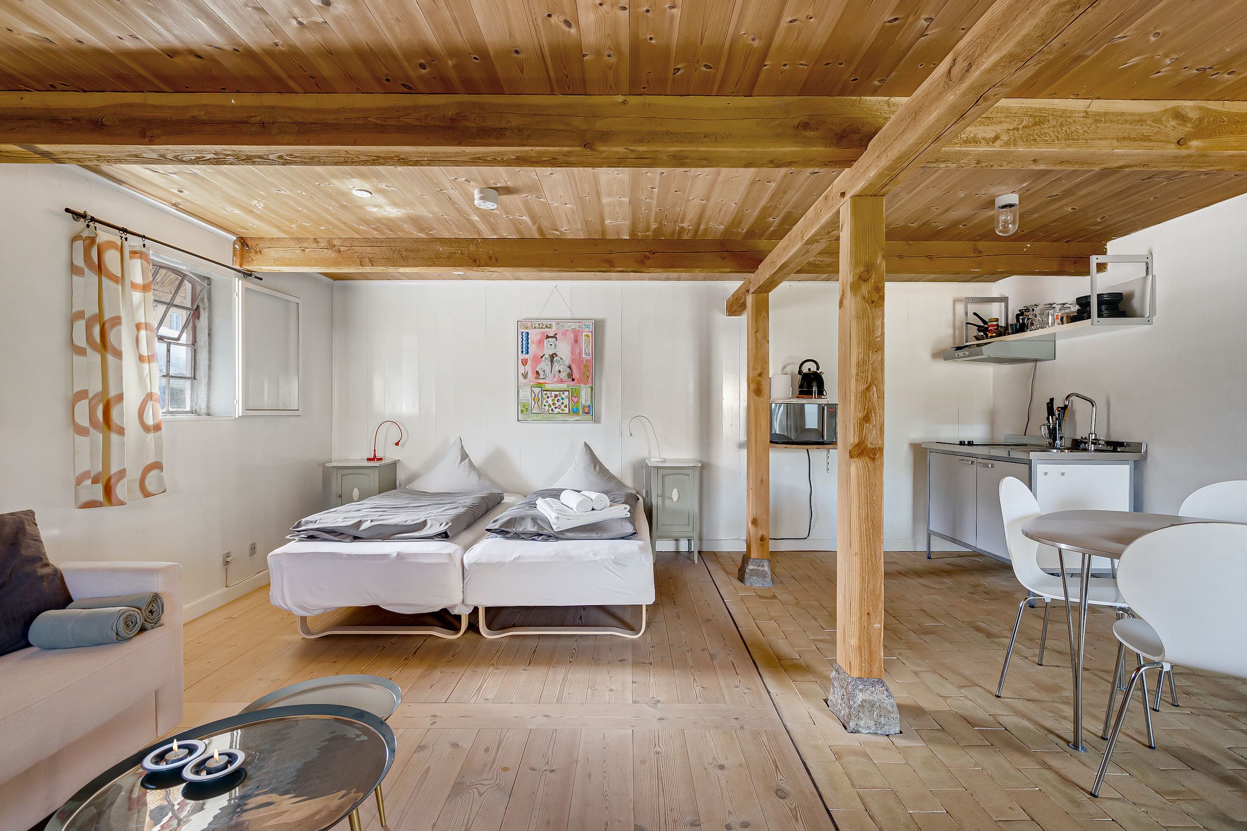 Hyggeligt værelse med 2 senge, komfortabel sofa, tekande, maleri og skovudsigt. Køkken med bord og stole, højtloftet og