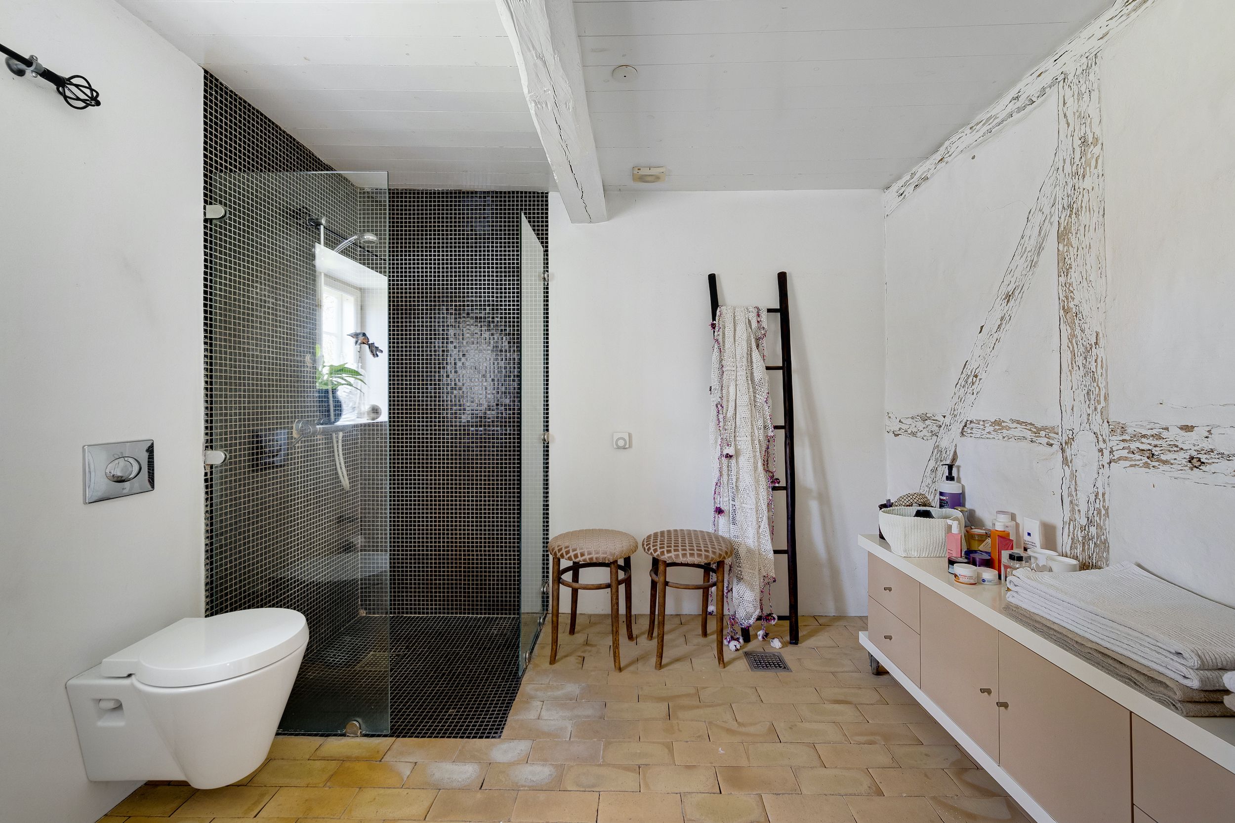 Et moderne badeværelse med badekar, bruserkabine, to barstole, hylde og et sæt håndklæder og kosmetik.