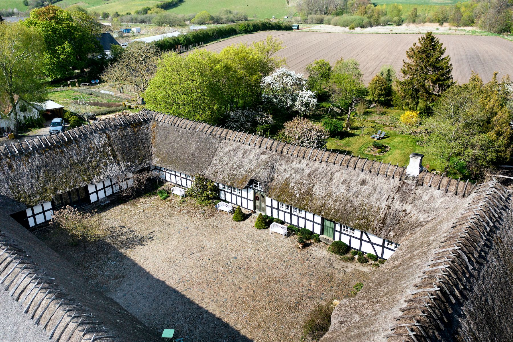 Fredet landejendom med stor nyttehave og parkområder, træhave med lænestole, udendørs badeområde og 2 huse med halmtag
