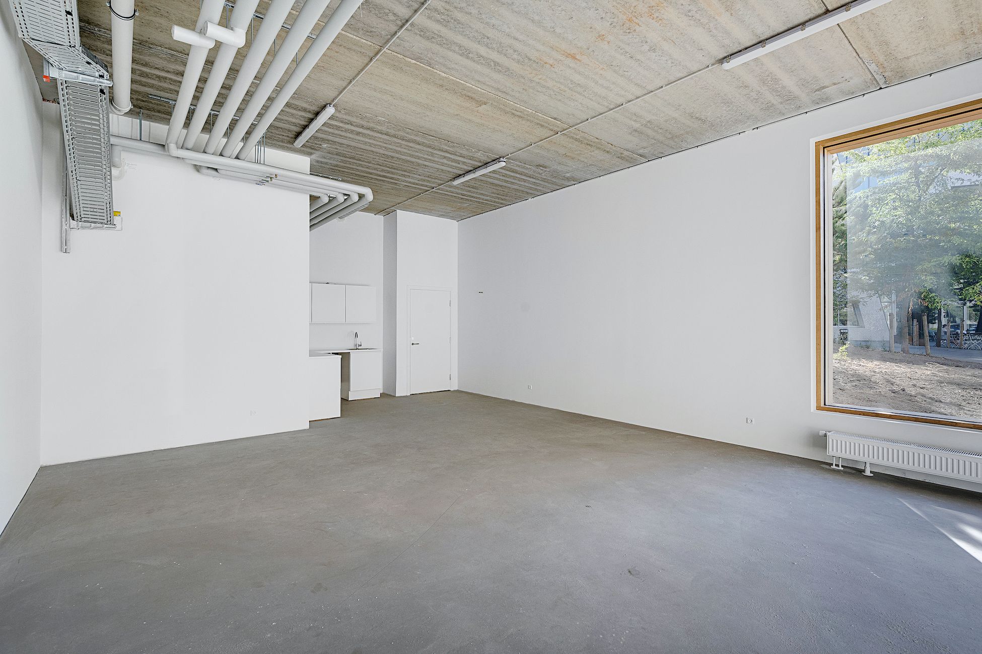 Et rum med hvide vægge og gulv, store vinduer og et køkken med højt skab og vask