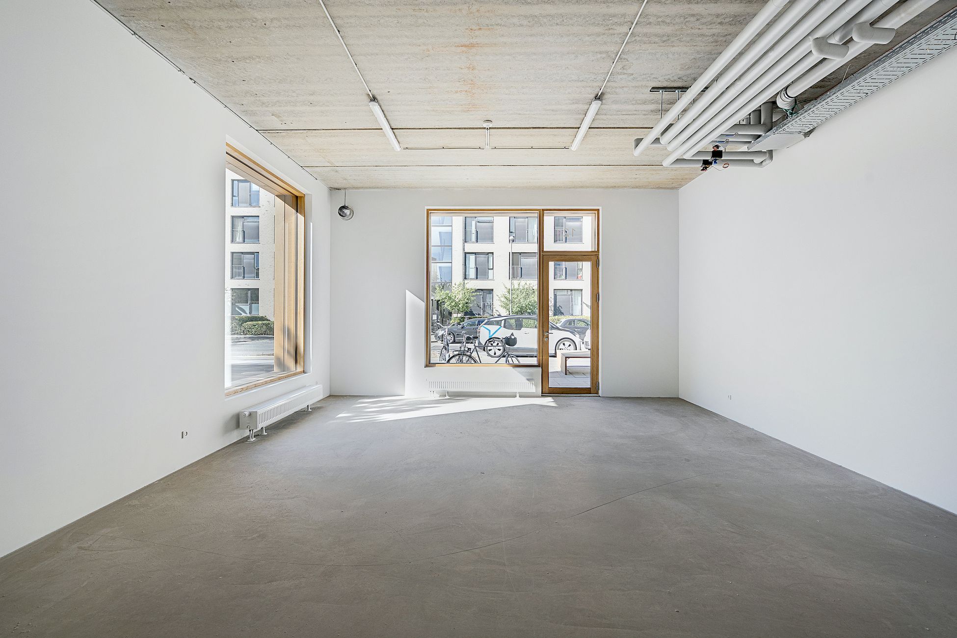 Et ubeboet og rummeligt værelse med hvide vægge, lysekroner og to store vinduer med træruder og døre