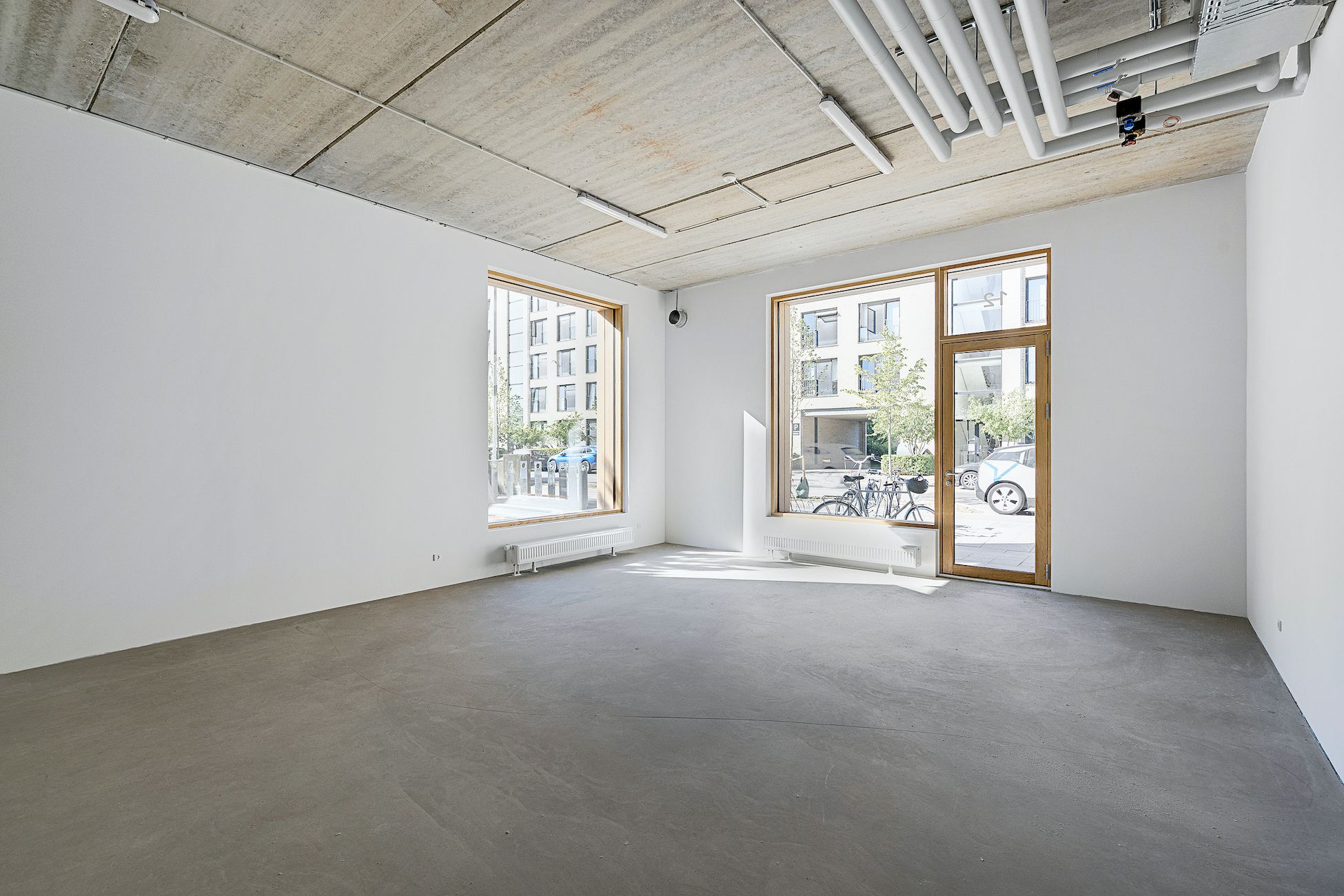 Et lejemål med en hvid væg og to store vinduer, hvor en cykel er parkeret udenfor