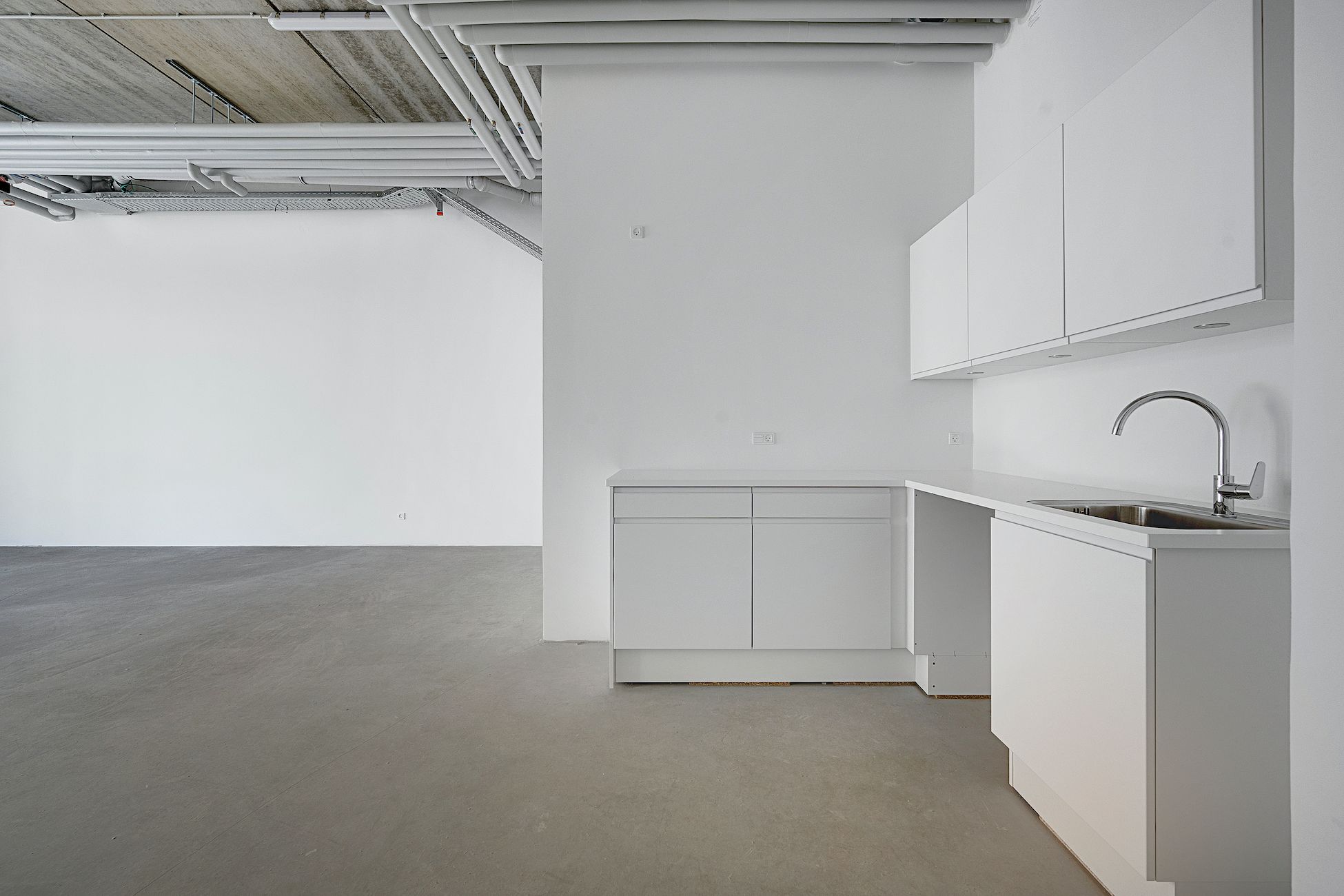 Moderne hvidt køkken med lysegrå gulv og loft med hvide rør og udstyr. Køkken med hvide vægge, hvide skabe og hvidt gulv.