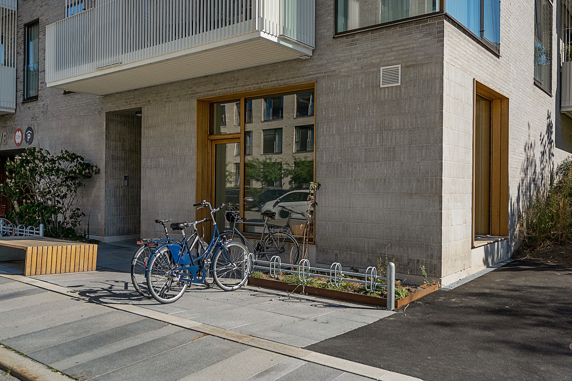 Bygning med moderne design, tre cykler parkeret udenfor og terrasse med udsigt over gaden