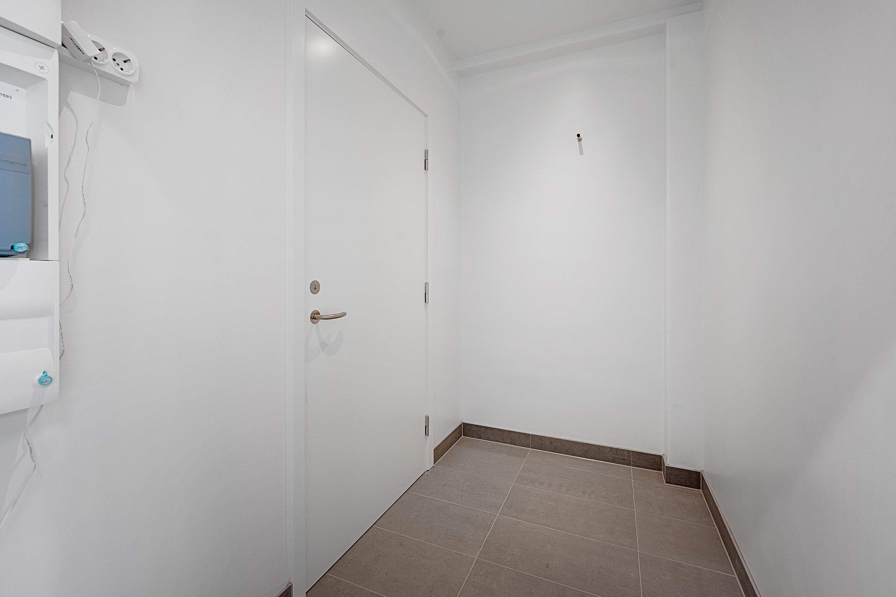 Et minimalistisk design med en hvid dør og vægge og en gulv med glat, gråt og beige farvede fliser