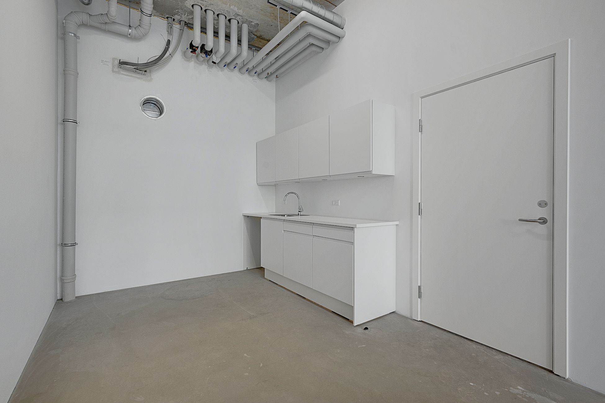 Rummelig og stilfuld køkken med hvide vægge og højloft. Moderne køkken med hvide skabe og en høj, hvid skraldsbage. Sorte