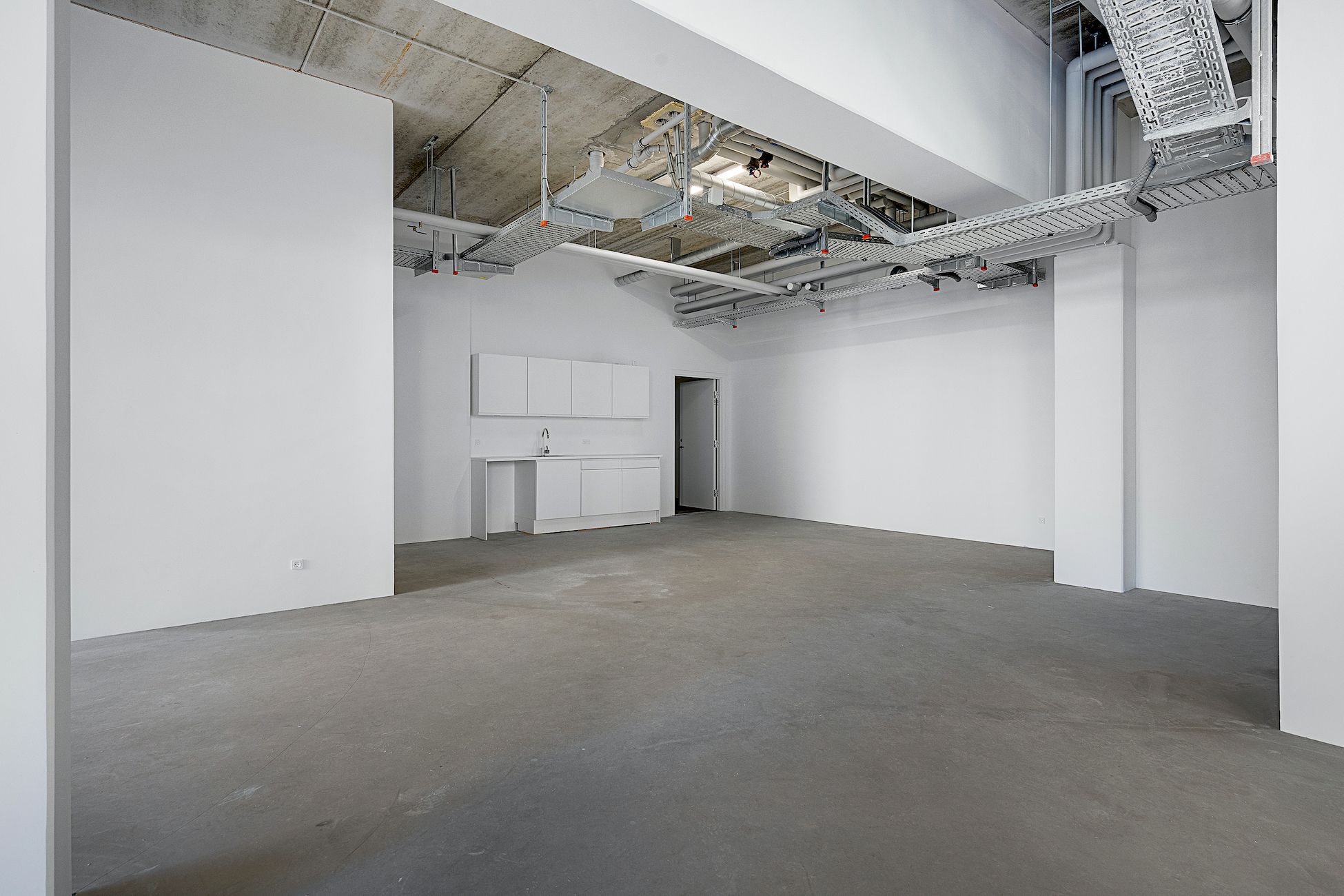En stor, tom og rummelig værkstedshal med hvide vægge og gulve samt hvide loftsreoler