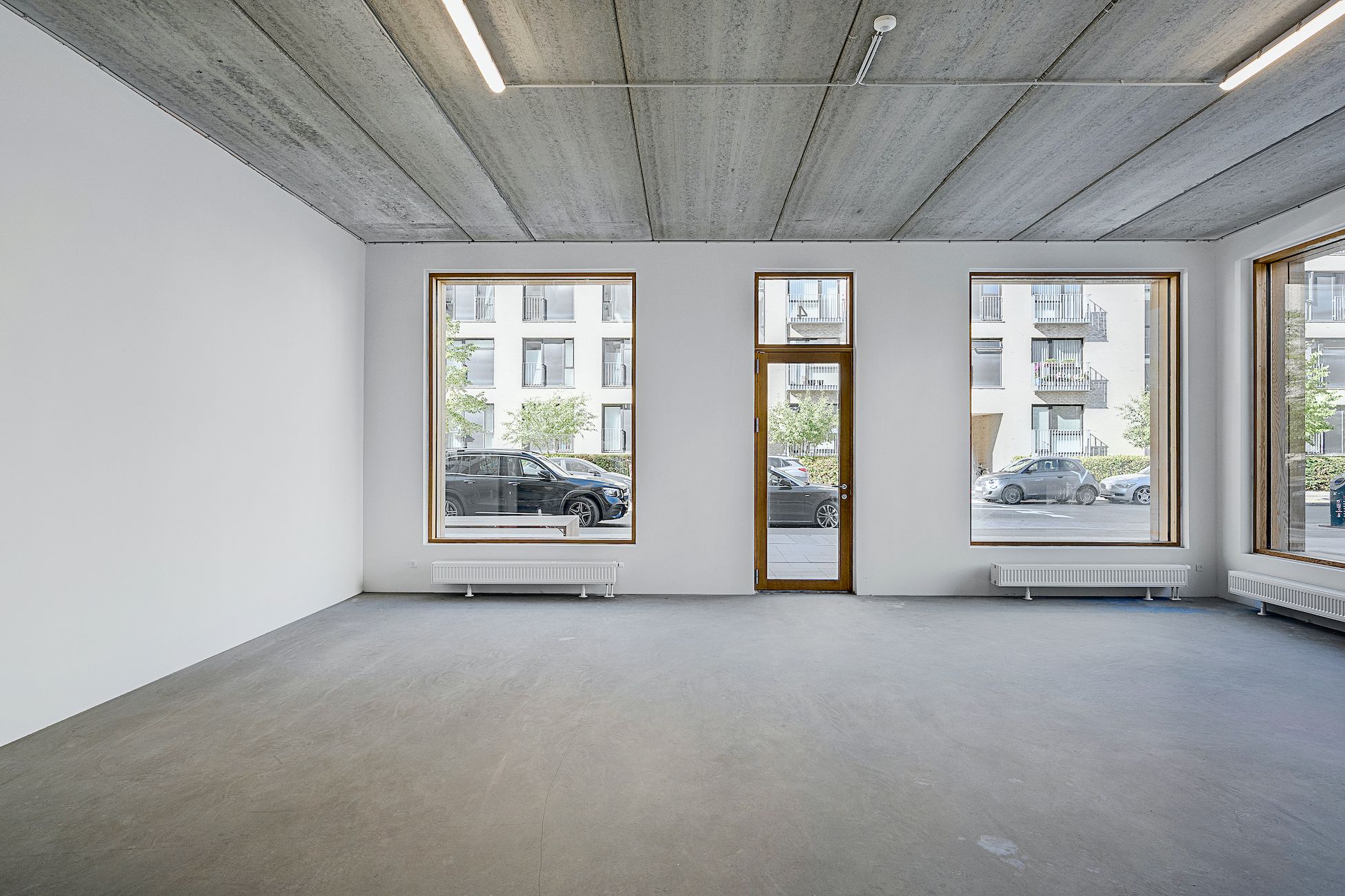 Et moderne kontor med hvide vægge og store vinduer og søjler i træ, der vender ud mod en parkeringsplads med biler og træer