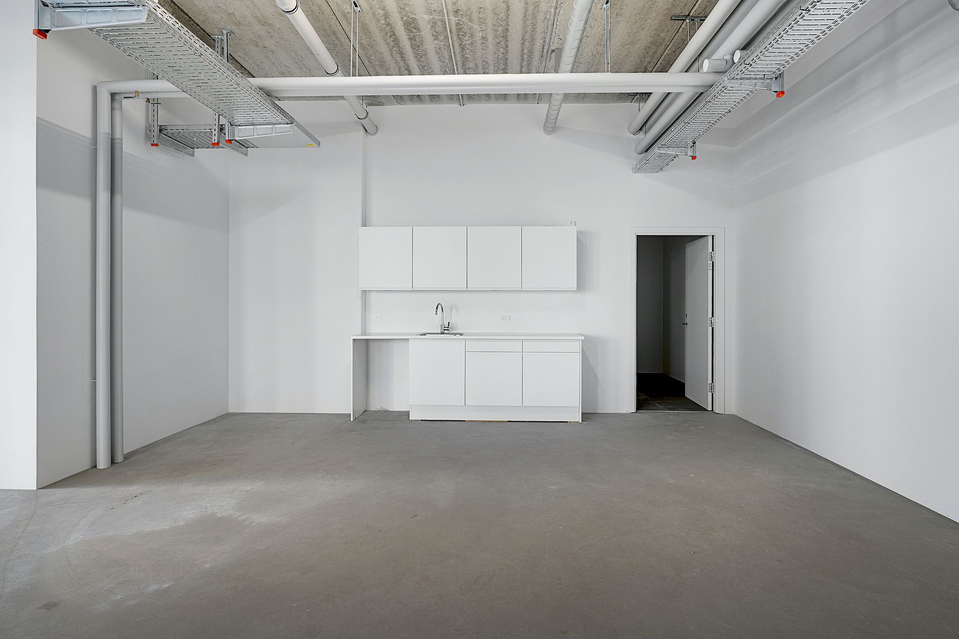 En tom værkstedslokal med hvide vægge, hvidt loft, hvide skabe og en hvid køkkenblok med vandhane og rent gulv