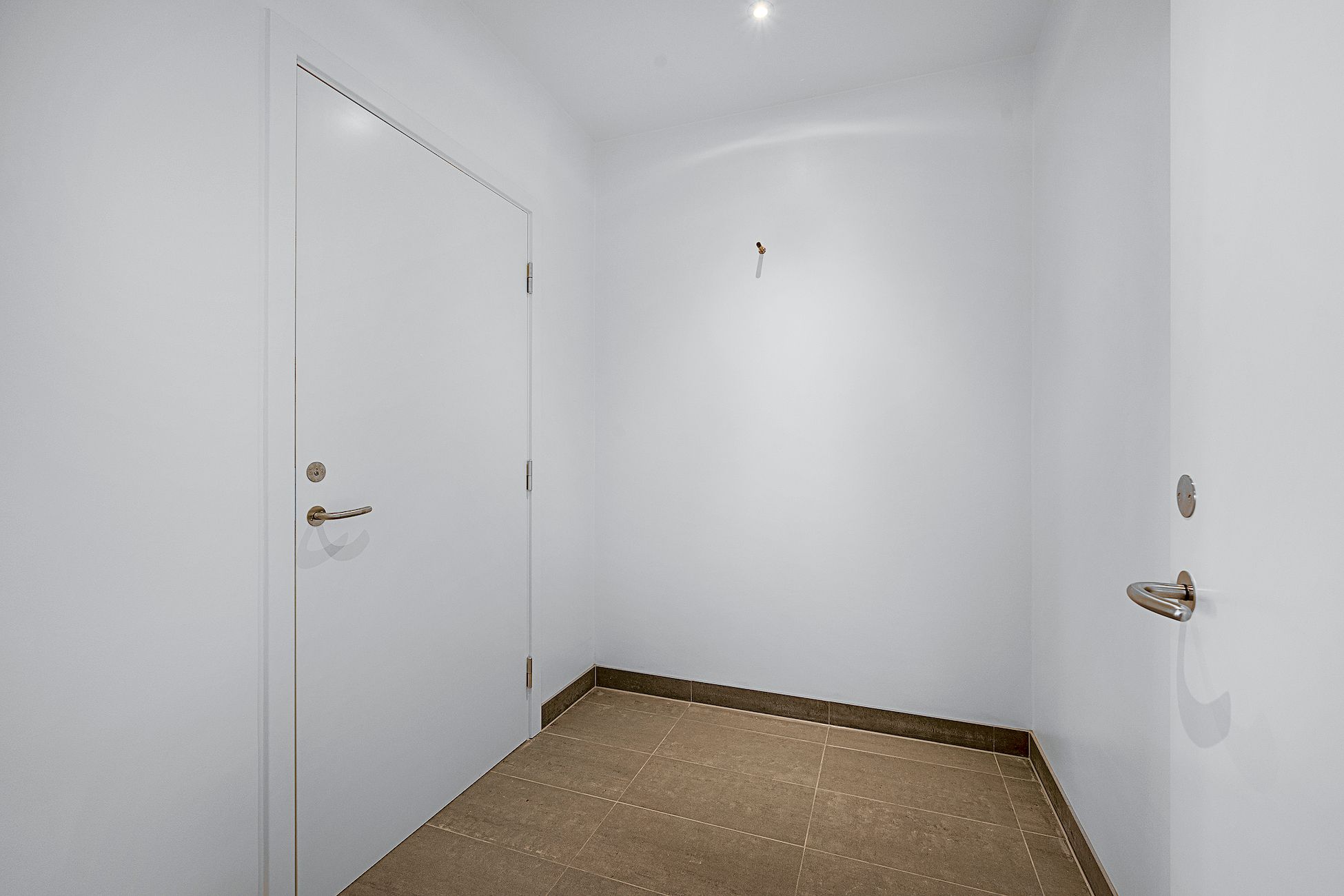 Rummet har hvide vægge og gulv og mørkegulve i en side. To døre er åbne og en dør er lukket. Der er også en dørbeslag og en