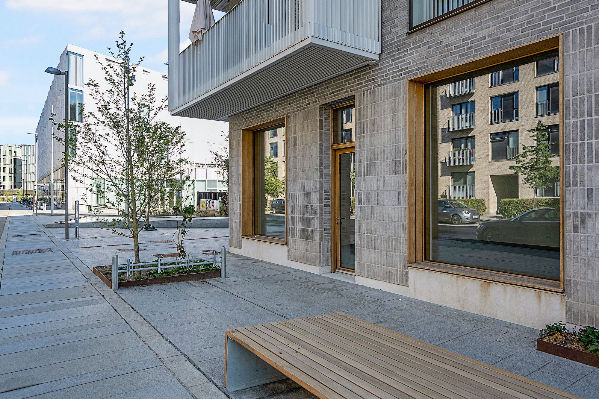 Et træ står på siden af en stenbro, og der er en lille terrasse med en plante. Bygningen har vinduer og er lavet af sten og