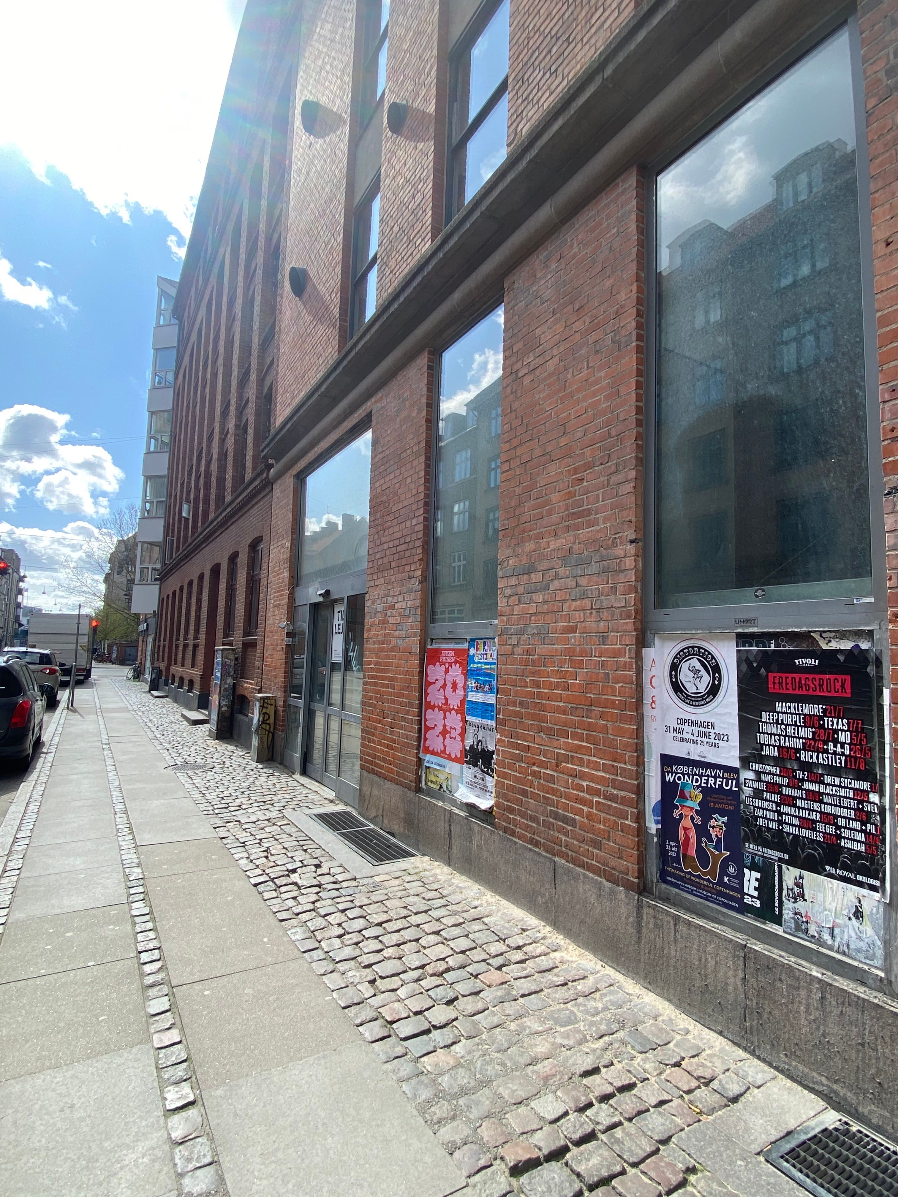 Gade med ny røde mursten og glasvinduer på et erhvervslejemål med reklameplakater på siderne