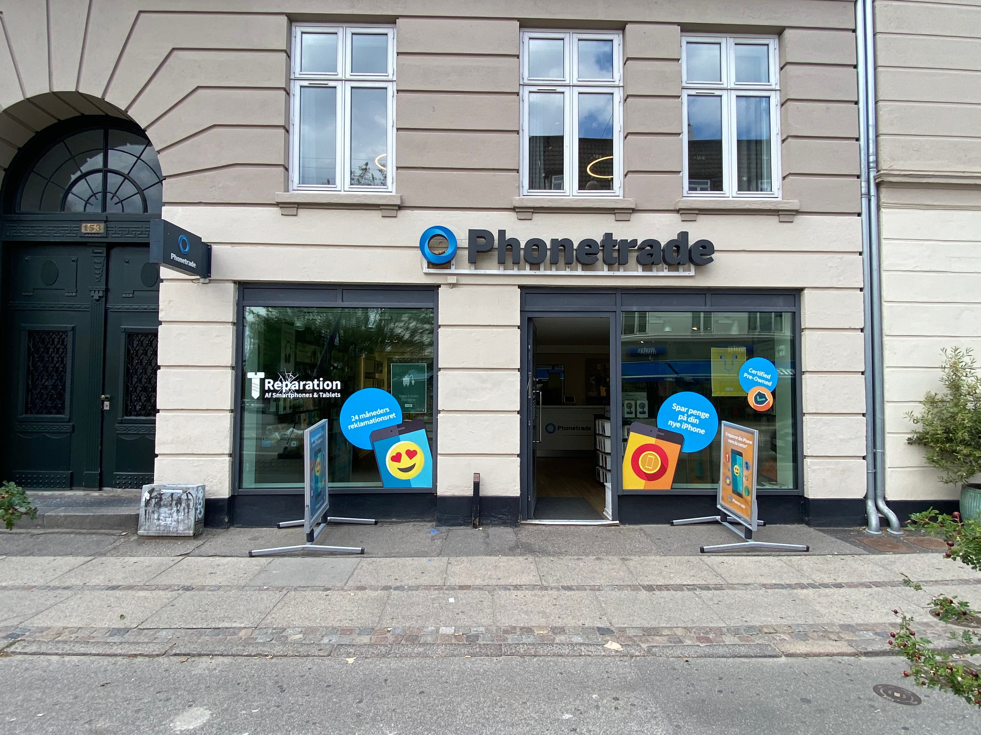 Foto af Phonetrade butik med reklameskilte på gaden i Danmark, med skrift, der siger reparation og 24 minutter